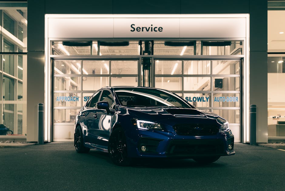 A stylish blue car is parked outside a modern service center at night, highlighting its sleek design and vibrant color.